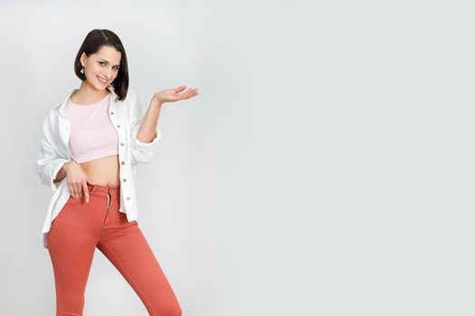 Cute brunette woman 30s in coral jeans, pink tank top and white shirt on white background. High key vertical shot with copy space