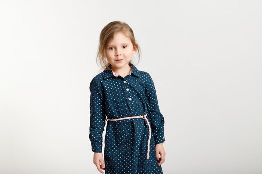 Little sweet caucasian fashion girl 4-6 years old wearing a blue dress with polka dots stands on a white background.