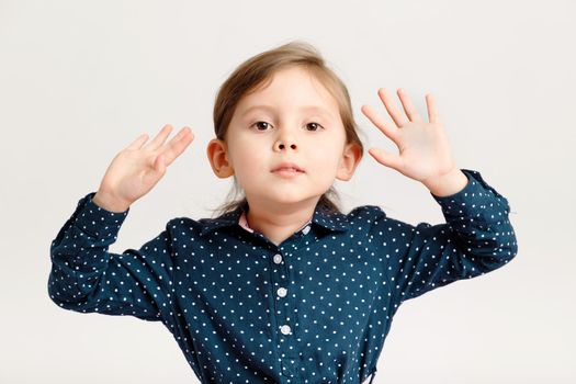Little sweet caucasian fashion girl 4-6 years old wearing a blue dress with polka dots standing with hand up. Cute kid girl on a white background