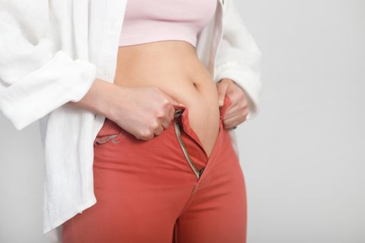 Close-up of belly fat woman can not fasten a zipper on jeans. Diet, overweight, obesity concept.