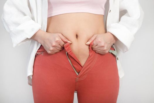 Close-up of stomach fat woman can not fasten a zipper on jeans. Diet, verweight, obesity concept.