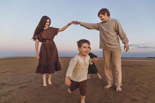 Young beautiful parents with two little cute children play and have fun in the evening on the seashore. Selective focus, grain effect