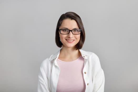 Portrait of mixed race, cheerful, modern, stylish, cute, clever, smiling woman in glasses on grey background, looking at camera