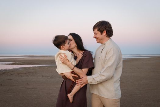 Happy young family have fun on beach hug and kiss at sunset. Family look natural clothes.