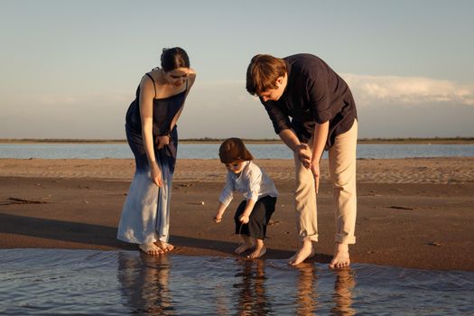 Little boy in brown hat spends time on the beach with his parents.