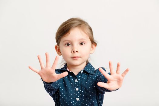 Little sweet caucasian fashion girl 4-6 years old wearing a blue dress with polka dots stretched her palms to the camera. Cute kid girl on a white background