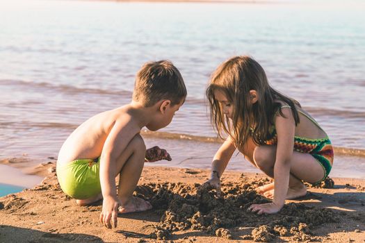 Boy and girl 3-5 years old playing with sand on the seashore.