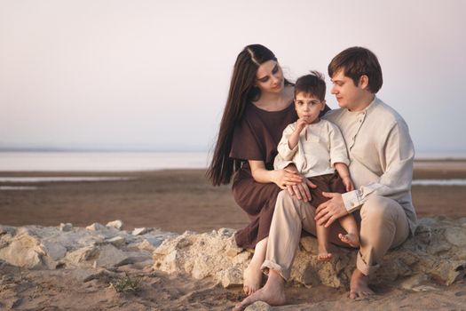 Young family of 3 people spend time together on the beach. Family look linen clothes. Copy space