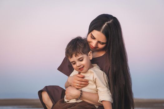 Tender portrait of a young mother with her little son. Golden hour shot at sunset outdoors.