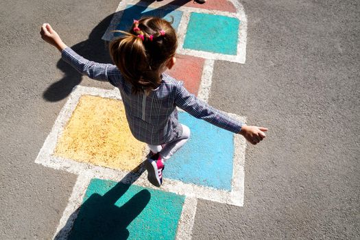 Kid girl 5 y.o. playing hopscotch on playground outdoors.