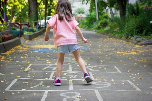 Little cute girl 5 y.o. playing hopscotch on playground outdoors. Selective soft focus