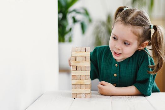 Little cute preschool girl plays at home with wood toys on table. Natural tactility development. Selective soft focus