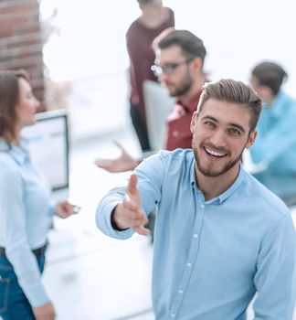 Handsome man looking at camera and smiling while his colleagues working in the background