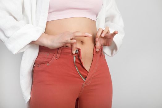 Close-up of belly young woman cannot wear summer pants. Diet, overweight, obesity concept.