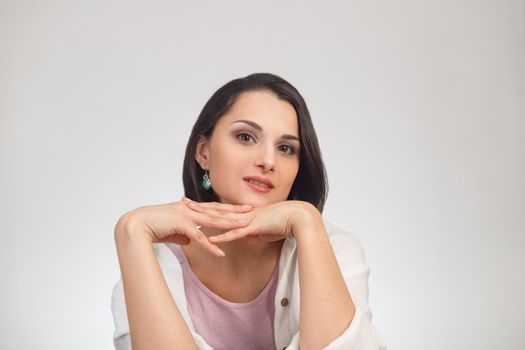 High-key studio portrait of a young brunette multiethnic woman in light clothes looking at camera.