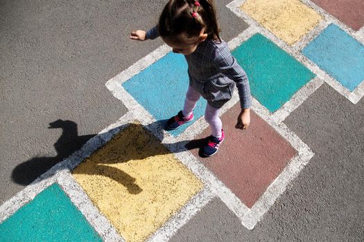 Kid girl 4 y.o. playing hopscotch on playground outdoors.