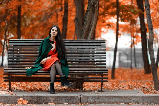 Young beautiful brunette bored alone on a bench in an autumn park.