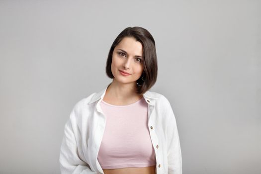 High key calm portrait of young brunette mixed race woman in pink tank and white shirt looking at camera.