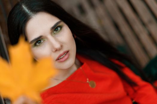 Portrait of a young woman in an orange dress with a yellow autumn leaf out of focus. Autumn tones and mood.