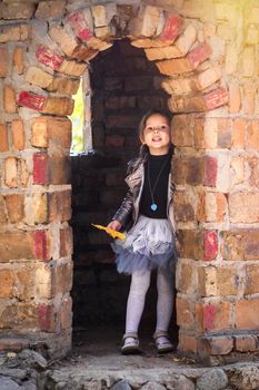 Little cute girl in trendy autumn clothes playing in the tower of the stone castle.