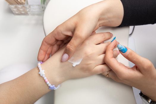 A manicurist applies hand cream to female hands after a hardware manicure in a beauty salon. Heart drawn on the hand, hand cream. Apply the cream to your hands. Hand care. Manicurist.