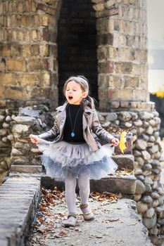 Little cute girl in fashionable autumn clothes sings on the background of a stone castle like a fairy princess.