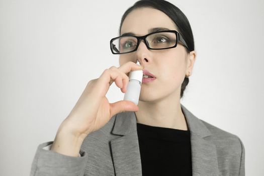 Young woman in glasses, using nasal spray.