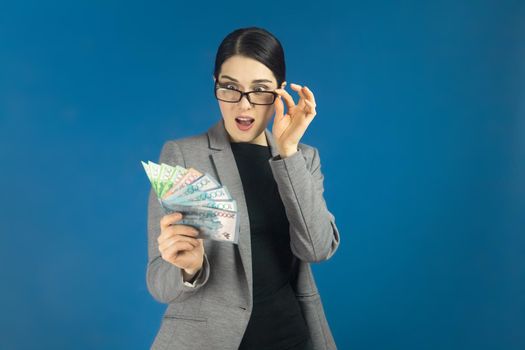 Young beautiful woman looks surprised at a pack of tenge in her hand. Selective focus.