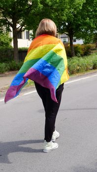 Bisexual, lesbian, woman, transgender stands with LGBT flag against blue sky with clouds on a sunny day and Celebrate Bisexuality Day or National Coming Out Day