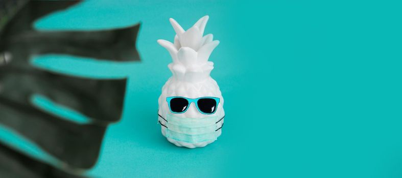 Pineapple in a medical mask and sunglasses on a turquoise background. Summer concept. Summer in Covid-19. Vision for the summer of 2020 during the coronavirus pandemic. Summer banner.