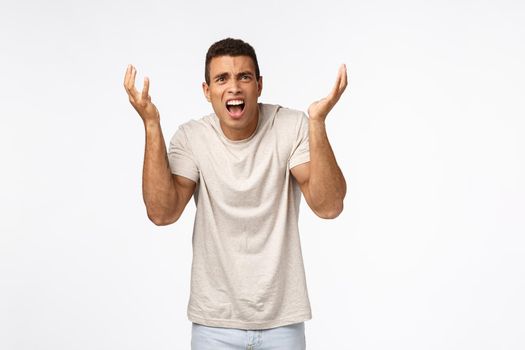 Disappointed and freak-out, bothered handsome man in t-shirt, raising hands up frustrated and displeased, arguing, complaining over unfair failure, losing competition, standing upset white background.