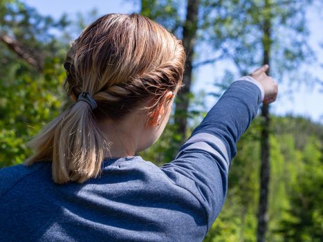 Woman shows direction in the forest. View from the back