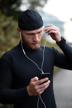 Close-up shot of young white man with beard putting headphone in his ear. Determined sportsman is ready for long-distance run and workout Athlete wearing sport fitness tracker and headphones.