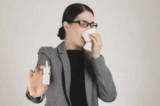 Allergy in a young woman in a gray jacket and glasses. Allergy nasal spray in hand. Selective focus.