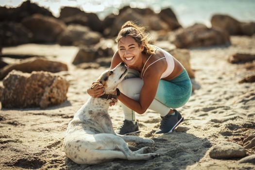 A beautiful young woman is petting her dear dog at the sea beach in summer sunny day.