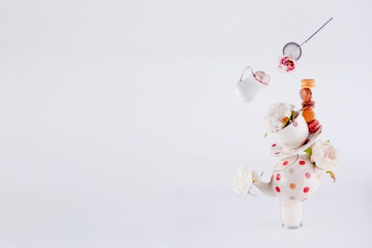 balancing structure of polka dot teapot, cup and saucers with macaroons and levitating milk jug and tea strainer blooming with flowers