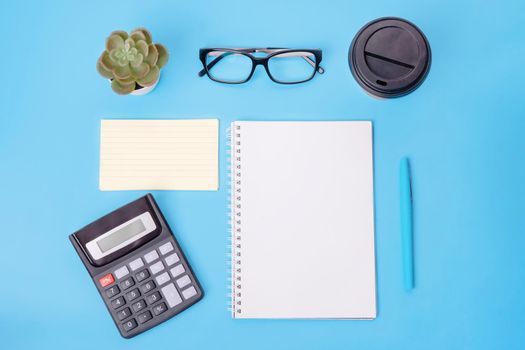 Calculator, blank, notepaper, piece of paper, coffee, glasses, plant and pen on blue background. workplace. Space for text. The financial checks