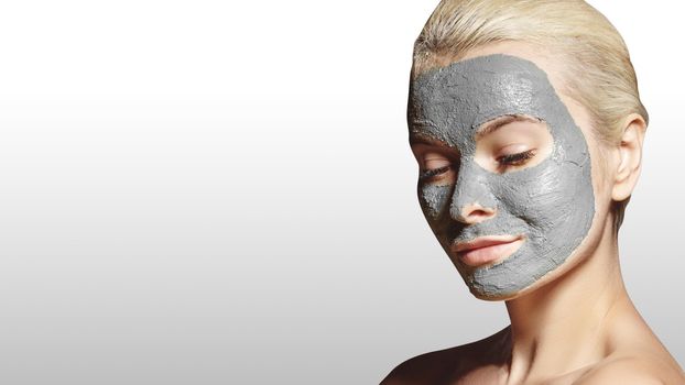Beautiful Woman Applying White Facial Mask. Beauty Treatments. Close-up Portrait of Spa Girl Apply Clay Facial mask on grey background.