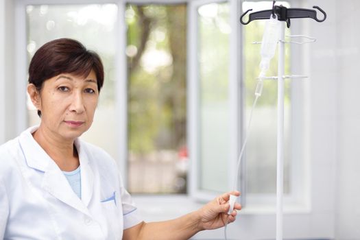 Portrait of a senior female nurse in middle asia Kazakhstan clinic intravenous drip hospital ward.