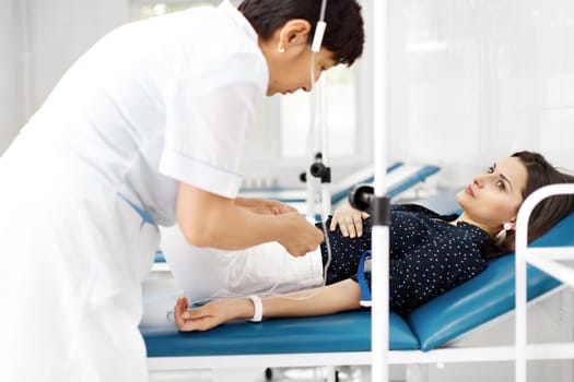 Nurse attaching intravenous tube to patient's hand in Kazakhstan clinic bed.