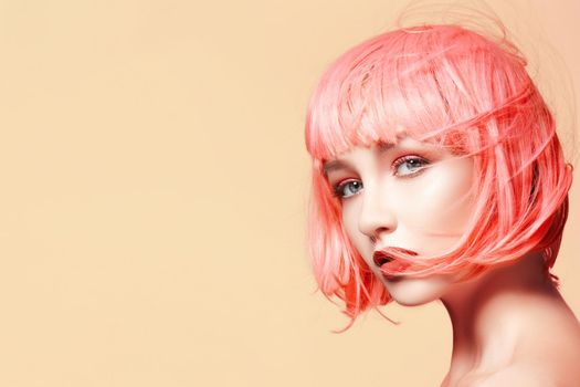 Young model in pink wig. Beautiful model with fashion makeup. Bright spring look. Sexy hair color, medium hairstyle on orange background