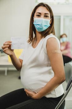 A pregnant woman showing vaccination certificate after receiving the Covid-19 vaccine. Looking at camera.