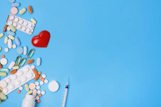 Pills, vitamins and disposable syringe, heart, stethoscope on blue background top view Space for text. see doctor.