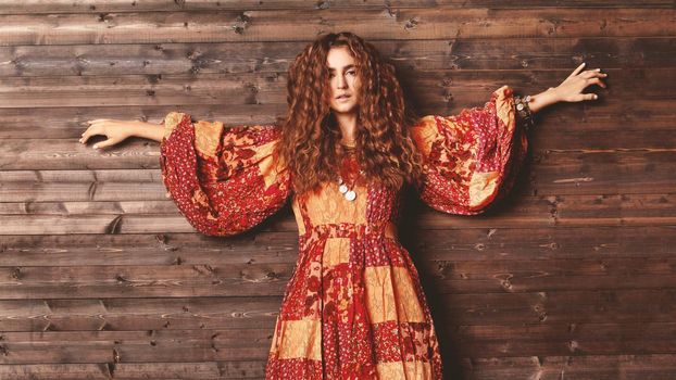 Beautiful young woman with long curly hairstyle and fashion jewelry. Hippie boho style clothes, long red dress. Flower children
