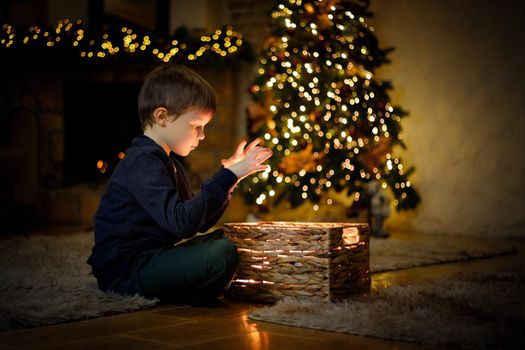 Little boy opened a magical New Year's gift in a Christmas interior with a Christmas tree and garlands. Selective soft focus, film grain effect