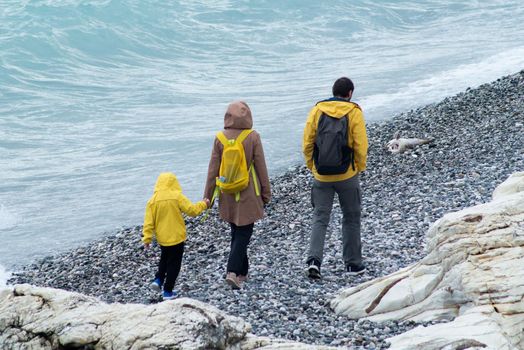 SOCHI, RUSSIA - MAY 09, 2022: a man, a woman and a child walk along a pebble beach in yellow raincoats