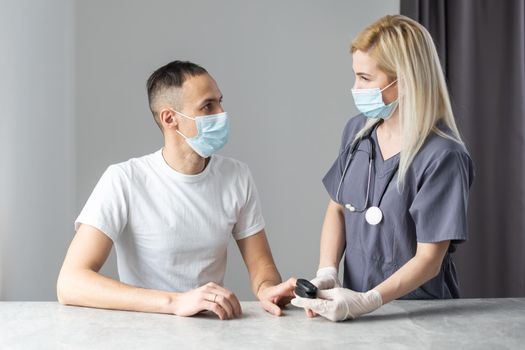 Doctor in purple uniform and shethoskope on a neck holds patient's hand with oximeter at patient's finger. White table. Medical concept.