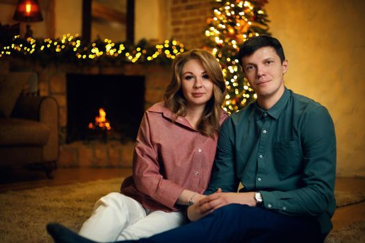 Beautiful middle aged caucasian couple posing in new year interior with a christmas tree and garlands. Selective soft focus, film grain effect