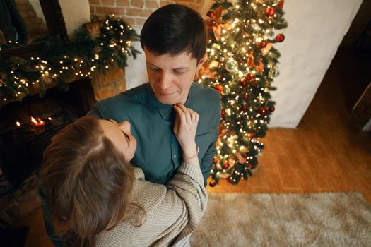 Beautiful middle aged caucasian couple look at each other in new year interior with a christmas tree and garlands. Selective soft focus, film grain effect