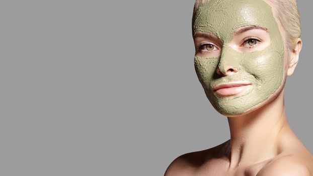 Beautiful Woman Applying Green Facial Mask. Beauty Treatments. Close-up Portrait of Spa Girl Apply Clay Facial mask on grey background.